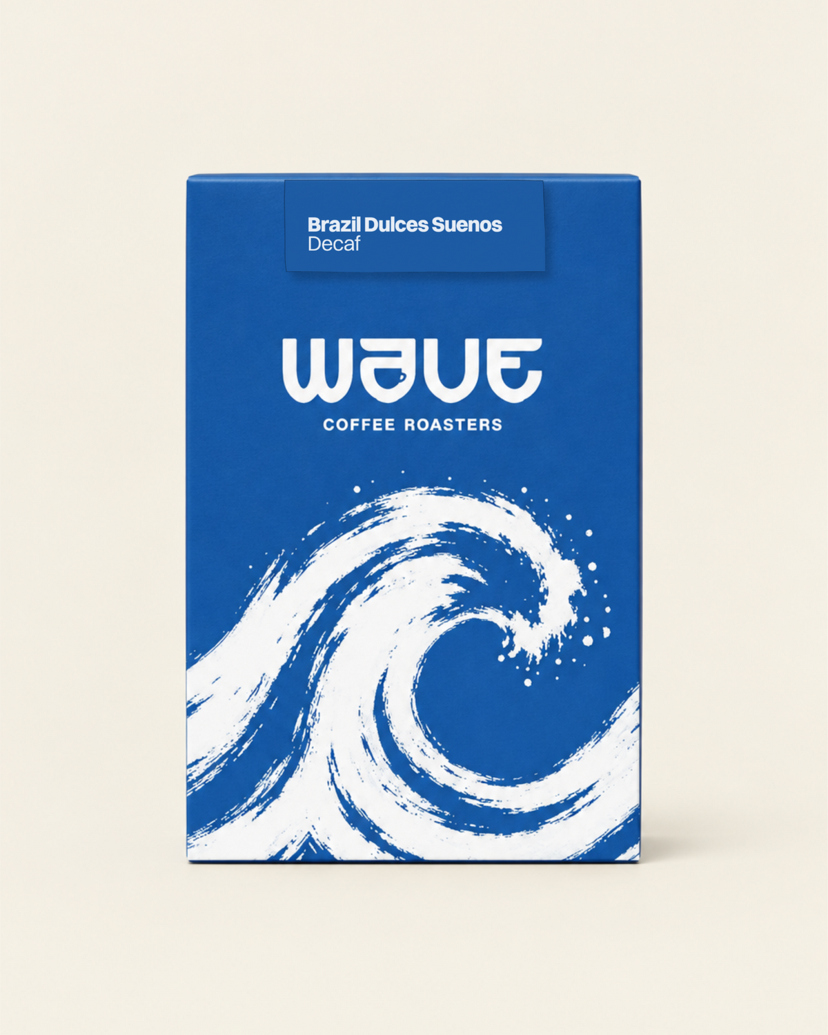 A rectangular coffee roaster box standing upright on a light beige background. The box has a blue or a dark blue design with a large white wave illustration and the visible brand name 'wave coffee roasters' with specialty coffee label: 'Brazil Dulce Suenos Decaf'