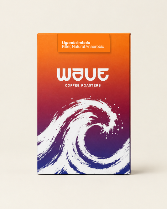 A rectangular coffee roaster box standing upright on a light beige background. The box has a bright orange-to-purple-to-blue gradient design with a large white wave illustration and the visible brand name 'wave coffee roasters' with specialty coffee label: 'Uganda Imbalu Filter, Natural Anaerobic'